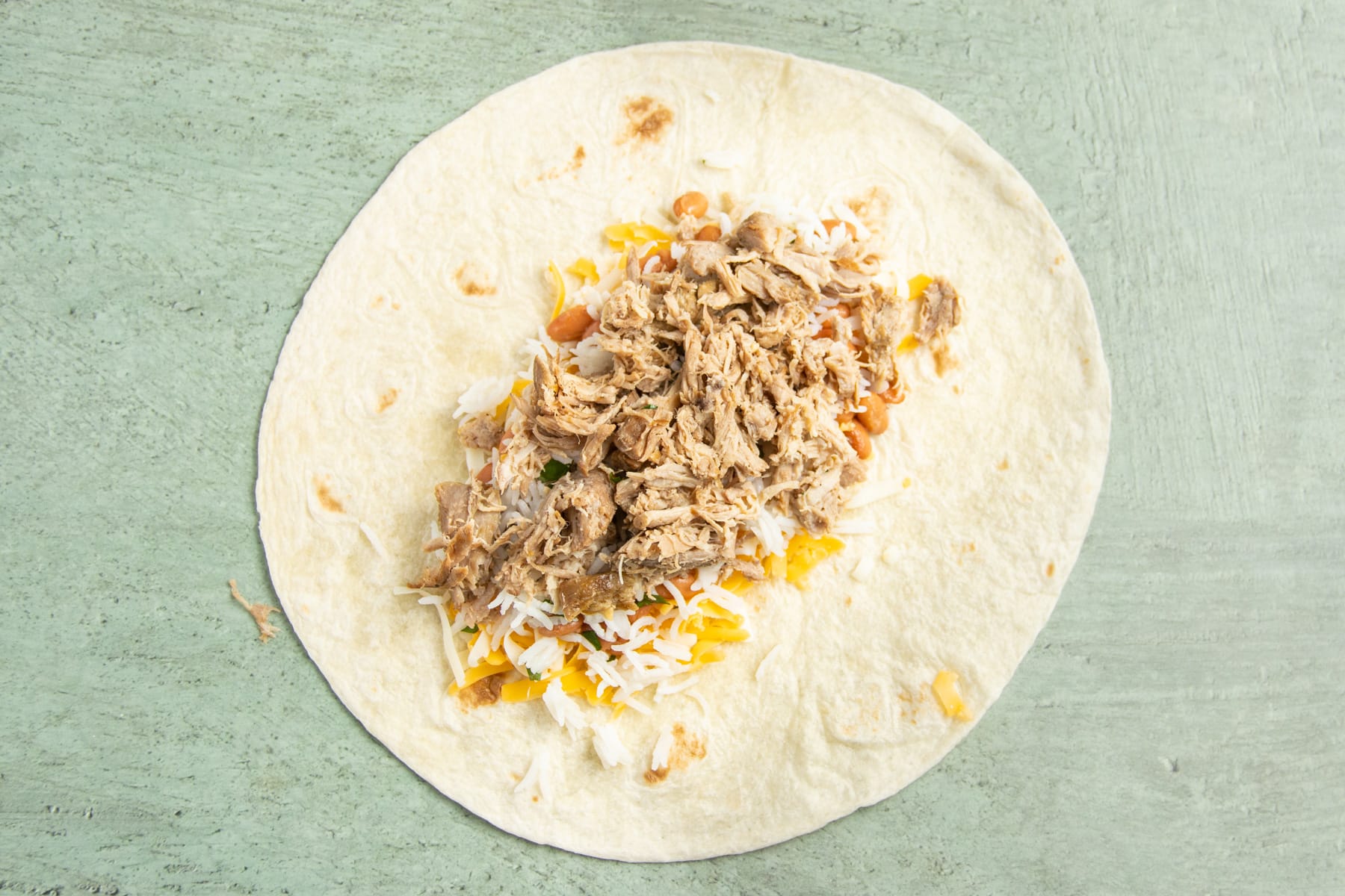 This is a picture of a large tortilla with carnitas added.