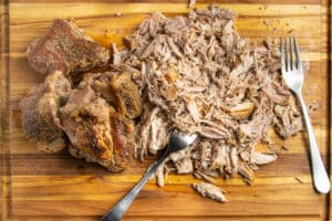 This is a picture of the slow cooker pork carnitas being shredded with fork on a cutting board.