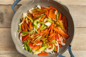 This is a picture of a skillet with peppers and onions cooking.